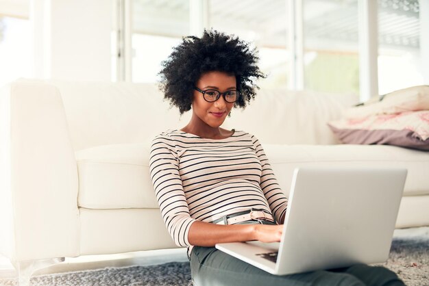 Sie verbringt einen Teil ihrer Freizeit online Schnappschuss einer jungen Frau, die zu Hause an ihrem Laptop arbeitet