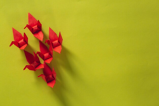 Sieben rote Origami-Vögel fliegen an der Spitze eines rosafarbenen Vogels, isoliert auf weißem, rotem Origami-Papierkranich