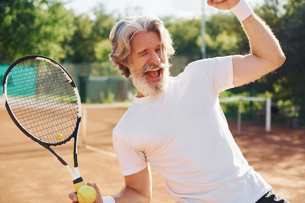 Sieg feiern Älterer, moderner, stilvoller Mann mit Schläger im Freien auf dem Tennisplatz tagsüber