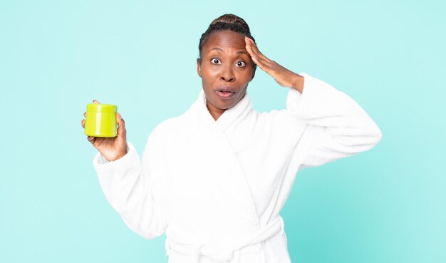 Sieht glücklich, erstaunt und überrascht aus, wenn man Bademantel trägt und eine Haarmaske hält