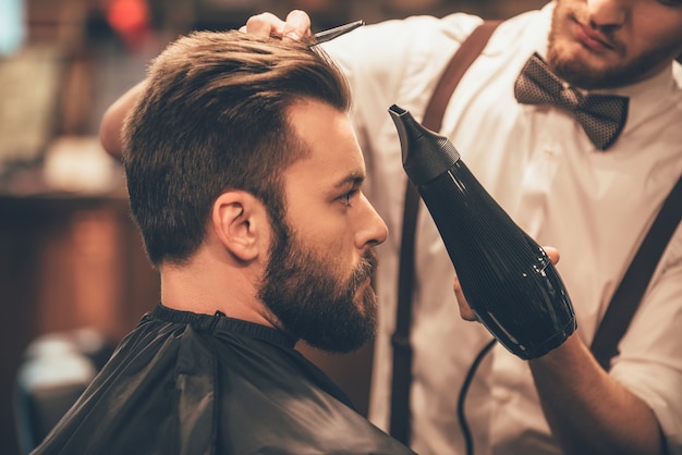 Sieht schon gut aus. nahaufnahme seitenansicht des jungen bärtigen mannes, der vom friseur gepflegt wird