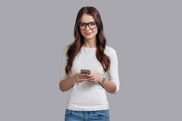 Siempre en contacto. Atractiva mujer joven en ropa casual con teléfono inteligente