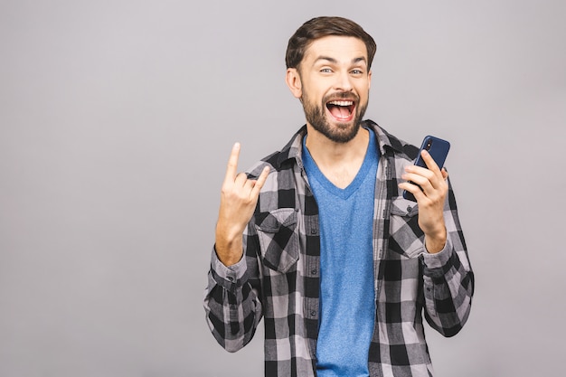 Siempre en contacto Hombre joven serio con teléfono inteligente. Retrato de un hombre joven feliz que usa el teléfono móvil aislado sobre la pared gris.