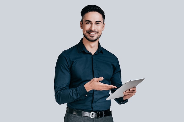 Foto siempre dispuesto a ayudar. apuesto joven en camisa apuntando a su tableta digital y sonriendo