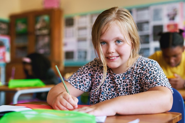 Siempre estoy ansiosa por aprender Fotografía de una niña sentada en su salón de clases en la escuela y escribiendo en su libro de trabajo