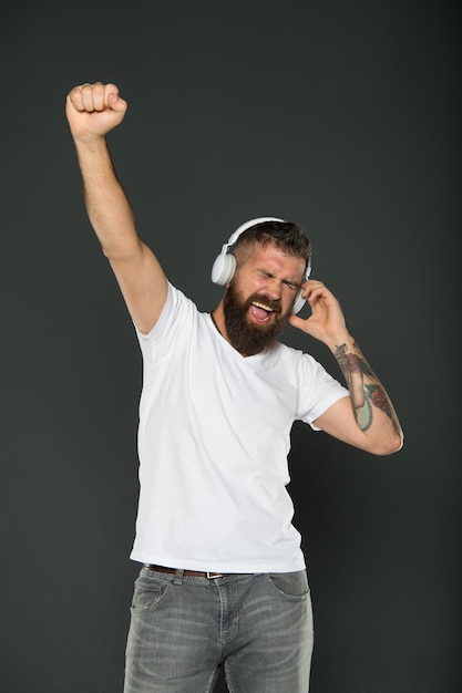 Siempre ganador Feliz ganador celebra con música Hombre barbudo con auriculares hace gesto de ganador Hipster emocional escucha música fondo gris Celebrando la victoria El ganador nunca se rinde