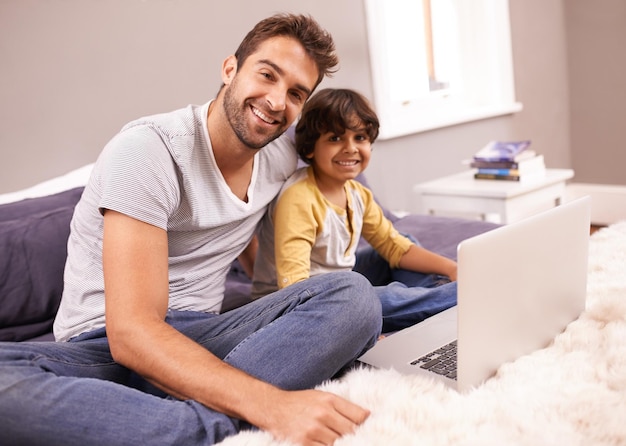 Siempre hay algo por lo que sonreír Retrato de un padre y su hijo sentados en la cama con su computadora portátil