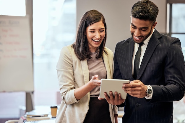 Siempre hay tiempo para una risa rápida Foto de dos jóvenes empresarios usando una tableta digital en el trabajo