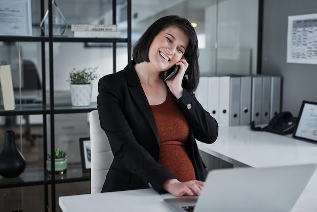 Siempre saludando a mis clientes con positividad Captura recortada de una atractiva mujer de negocios embarazada sentada sola en la oficina y usando tecnología