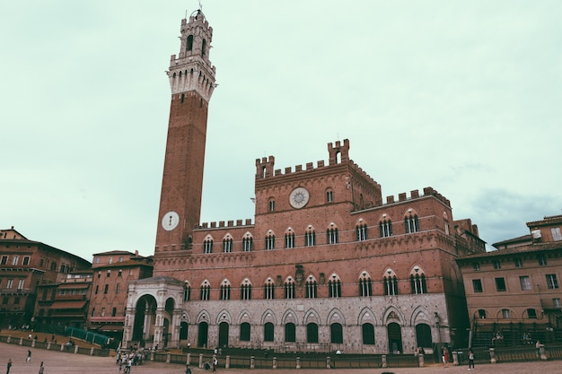 Siena, Itália - 28 de junho de 2018: Vista panorâmica do Palazzo Pubblico (Câmara Municipal) é um palácio e Torre del Mangia é uma torre na cidade na Piazza del Campo. Dia ensolarado de verão e céu azul dramático