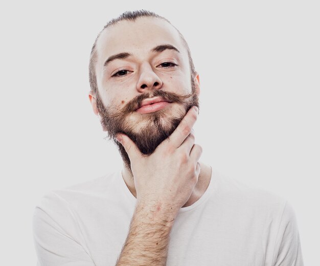 Siendo serio Hombre barbudo concentrado con una camisa blanca y un arete y tocándose la barbilla mientras piensa