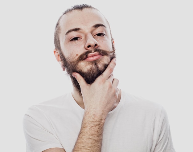 Siendo serio Hombre barbudo concentrado con una camisa blanca y un arete y tocándose la barbilla mientras piensa