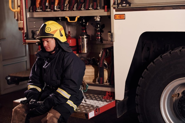 Se sienta en el camión Bombero masculino con uniforme de protección Se siente cansado