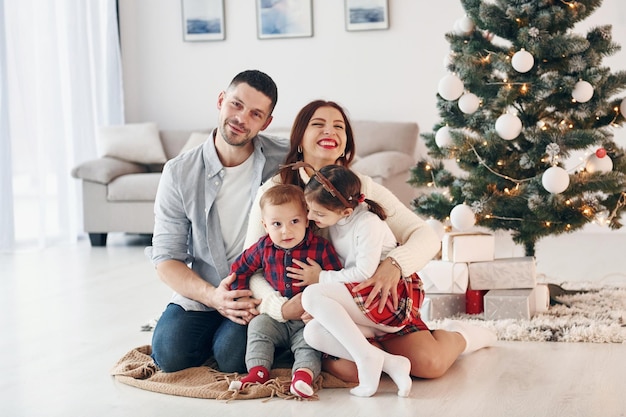 Se sienta contra el abeto Hermosa familia celebra el Año Nuevo y la Navidad en el interior de su casa