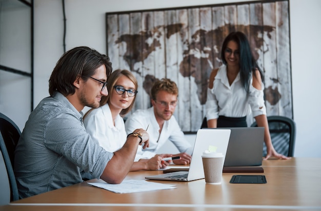 Se sienta junto a la mesa con computadoras portátiles. Jóvenes empresarios en ropa formal que trabajan en la oficina.