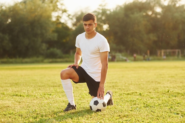 Se sienta en la rodilla con balón Joven futbolista tiene entrenamiento en el campo deportivo