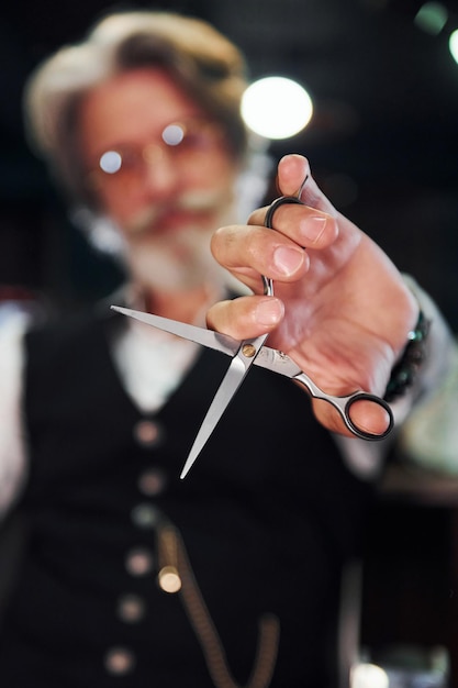 Se sienta en la silla en la barbería Elegante hombre senior moderno con cabello gris y barba está en el interior