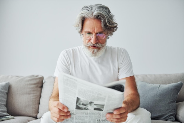 Se sienta en el sofá Hombre moderno con estilo senior con pelo gris y barba en el interior