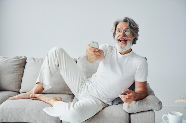 Se sienta en el sofá Hombre moderno con estilo senior con pelo gris y barba en el interior