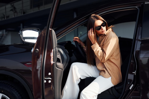 Se sienta con la ventana del auto abierta Moda joven hermosa y su automóvil moderno