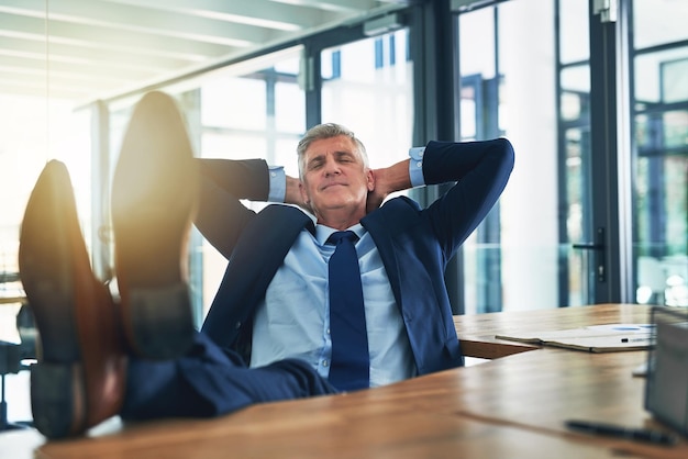 Se siente bien ser el jefe Foto de un hombre de negocios satisfecho relajándose con los pies sobre su escritorio