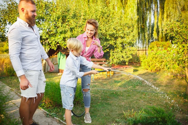 Se siente cómodo. Familia feliz durante el riego de plantas en un jardín al aire libre. Amor, familia, estilo de vida, cosecha, concepto de otoño. Alegre, sana y encantadora. Alimentos orgánicos, agricultura, jardinería.