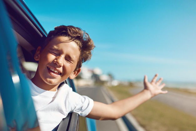 Siente el viento en tu cabello y en tu cara Fotografía de un niño feliz asomado a la ventanilla del auto en un viaje a la playa