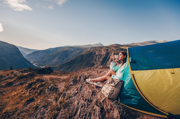 Siéntese cerca de la carpa de entrada con una taza de té y disfrute de la hermosa vista de las montañas. Una joven con una sudadera con capucha azul disfruta del ambiente.