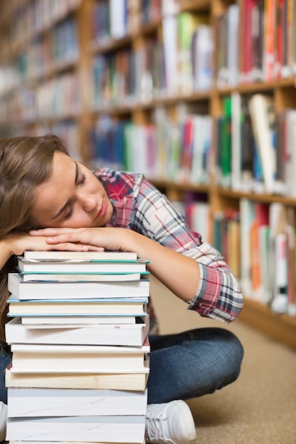 Siesta estudiante sentada en el piso de la biblioteca apoyándose en la pila de libros