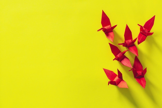 Siete pájaros origami rojos vuelan liderados por un pájaro rosa, aislados en una grulla de papel origami blanca y roja