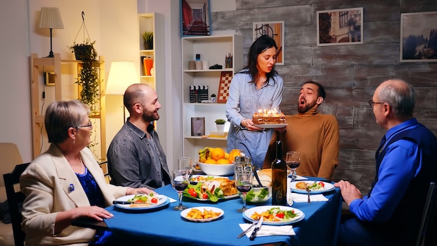 Siga la foto de una mujer joven con pastel de cumpleaños para su hermano en la cena familiar.