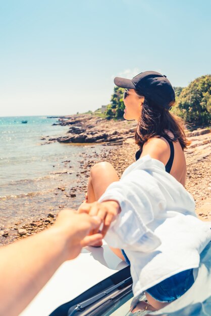 Siga-me conceito mulher sentada no capô do carro descansando na praia