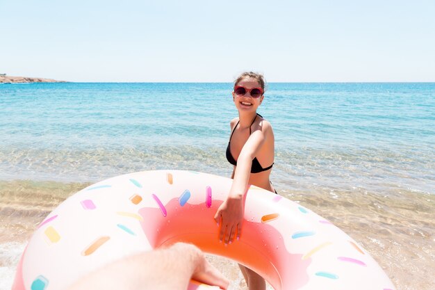 Siga-me o conceito de férias. garota chama para nadar no mar e acena com a mão. Menina relaxando no anel inflável no mar. Férias de verão.