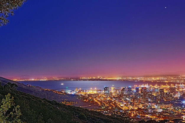 Signal Hill na Cidade do Cabo África do Sul com copyspace contra o fundo do céu noturno escuro e a vista de uma cidade costeira Paisagem panorâmica cênica de luzes iluminando um horizonte urbano ao longo do mar