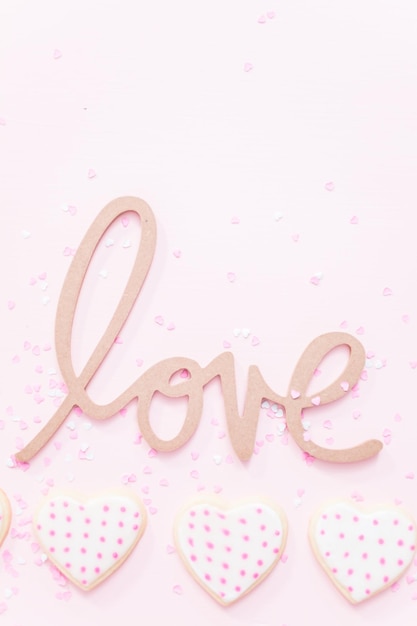Signo de AMOR con galletas de azúcar en forma de corazón sobre un fondo rosa.