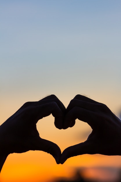 Signo de amor. Símbolo del corazón a mano silueta en el cielo al atardecer