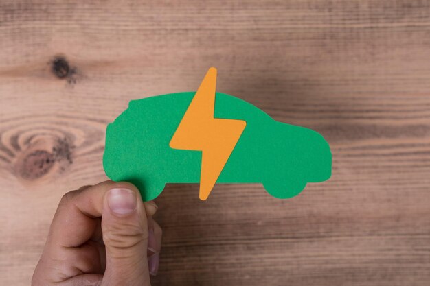 Signo de la electricidad en el corte de papel de un coche en las manos de un hombre