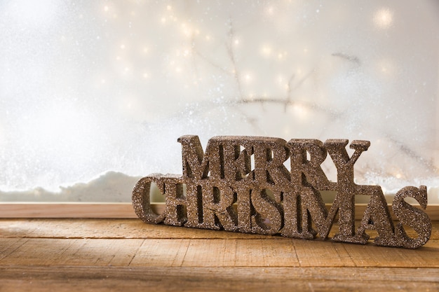 Signo de feliz Navidad en la mesa de madera cerca del banco de nieve y luces de hadas