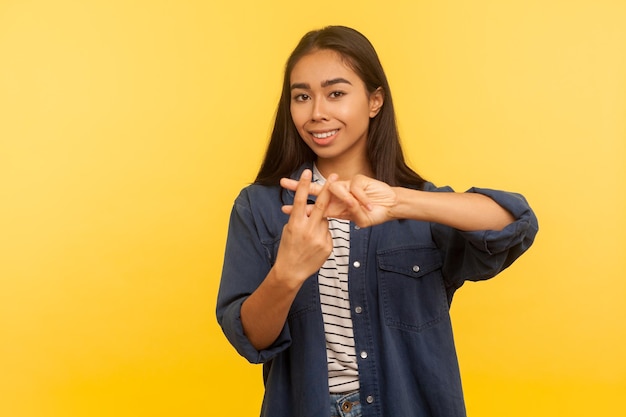 Signo de hash cruzó los dedos Retrato de niña feliz en camisa de mezclilla haciendo gesto de hashtag símbolo web de tema viral famoso comentario y blogueando tiro de estudio interior aislado sobre fondo amarillo