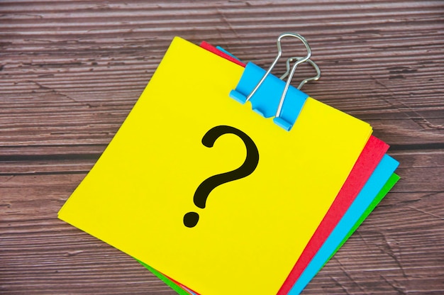 Signo de interrogación en el bloc de notas amarillo con fondo de escritorio de madera Concepto motivacional
