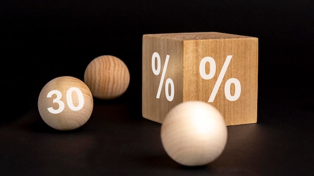 Signo de porcentaje en cubo de madera sobre fondo negro con bolas de madera número 30 en concepto de venta y descuento de bolas de madera