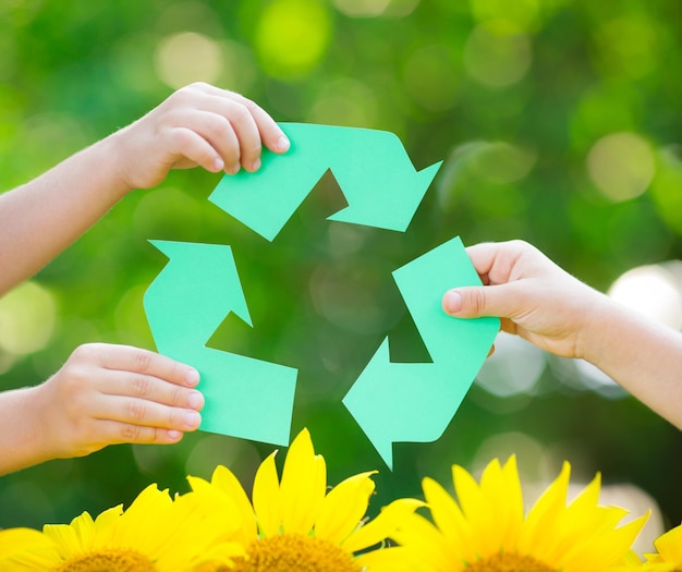 Signo de RECICLAJE de papel en las manos contra el fondo verde de la primavera Concepto del día de la tierra