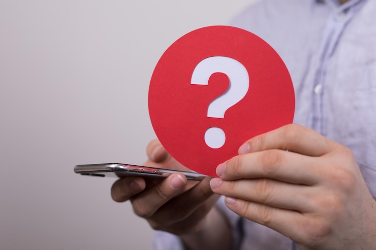 Foto signo del signo de interrogación hecho de papel rojo y teléfono inteligente en manos de un hombre