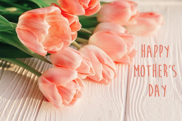 Signo de texto del día de la madre feliz en tulipanes rosados sobre fondo blanco de madera rústica concepto de tarjeta de felicitación imagen de mujeres tiernas sensuales flores de primavera en la suave luz del sol de la mañana