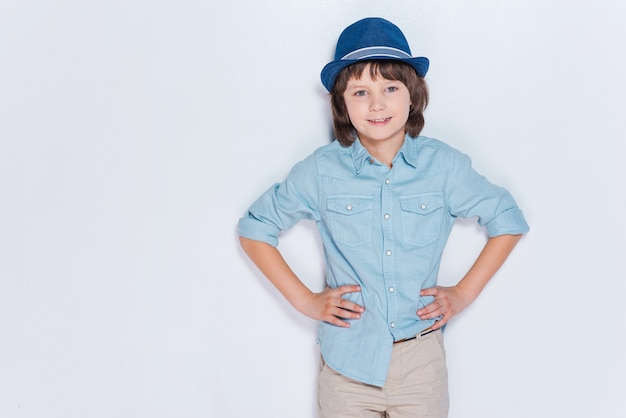 ¡Sigue así! Niño alegre con sombrero y tomados de la mano en las caderas mientras está de pie contra el fondo blanco.