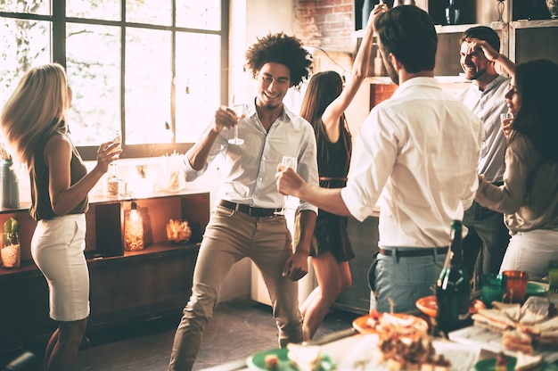 ¡Sigue bailando! Jóvenes alegres bailando y bebiendo mientras disfrutan de la fiesta en casa en la cocina