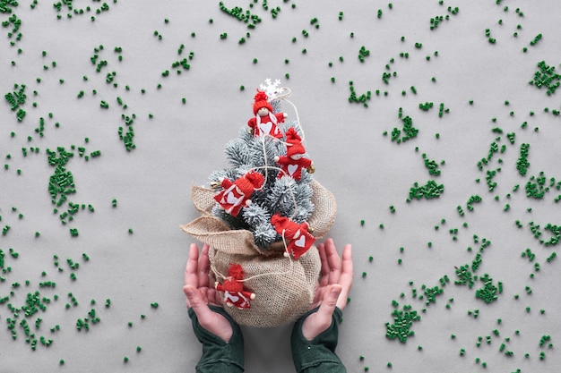 Sigue usando tu falso árbol de Navidad falso el mayor tiempo posible. Concepto de Navidad verde ecológico alternativo. Las manos muestran un árbol de plástico envuelto en una malla de arpillera con partículas de plástico sobre papel artesanal marrón.