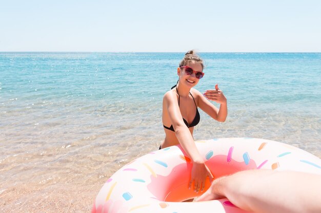 Sígueme el concepto de vacaciones. la mujer llama a nadar en el mar y agita la mano. Chica relajante en anillo inflable en el mar. Vacaciones de verano.