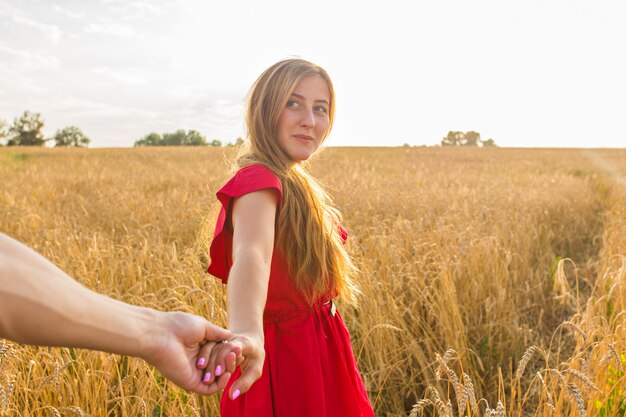 Sígueme, hermosa joven sostiene la mano del hombre en un campo de trigo