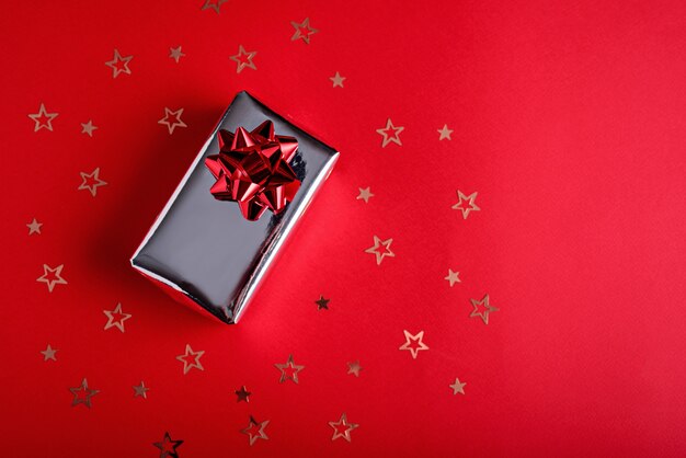 Silber Geschenkbox mit roter Schleife mit goldenen Sternen Pailletten auf rotem Hintergrund mit Kopienraum